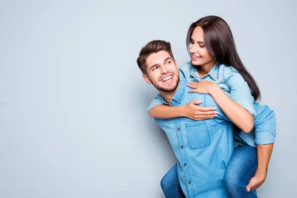 Homem feliz carregando sua namorada nas costas em backgroun cinza — Fotografia de Stock