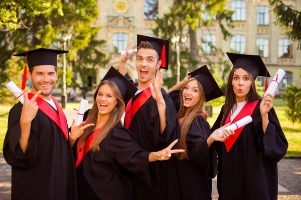 Exitosos excitados cinco graduados en túnicas de pie en fila y s —  Fotos de Stock