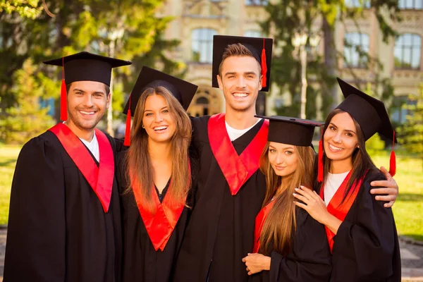 Éxito alegre cinco graduados en túnicas y sombreros sonriendo y h —  Fotos de Stock