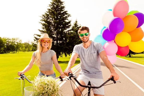 Jonge gelukkige paar met ballonnen op een fiets rijden in het park — Stockfoto