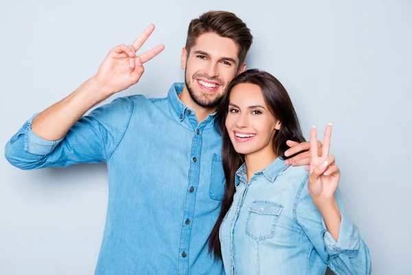 Dva šťastní mladých milenců v džínách, všeobjímající a ukázal v-sign — Stock fotografie