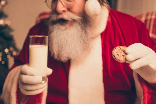 Close up of aged Santa holding chocolate cookie and glass of mil — Stock Photo, Image