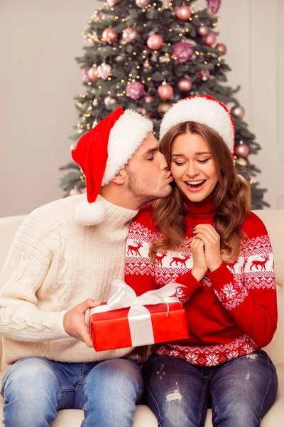 Schöner Mann mit Weihnachtsmütze, der seiner Freundin ein Weihnachtsgeschenk macht — Stockfoto