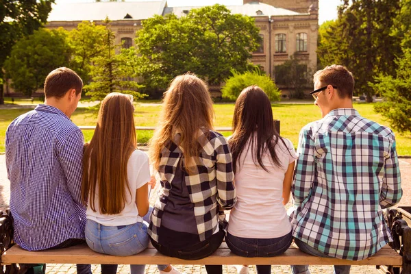 Вид ззаду фотографія п'яти різноманітних студентів, що сидять на лавці і вул — стокове фото