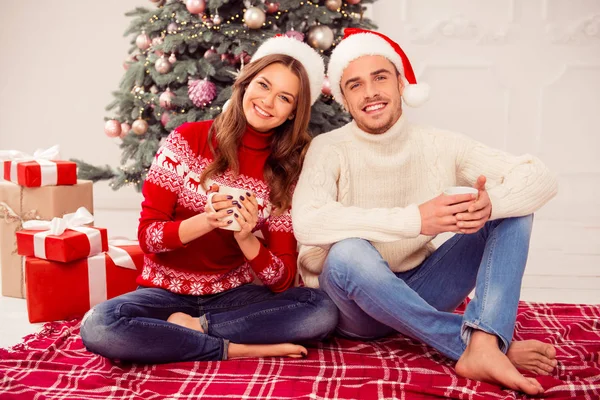 Ελκυστικά χαρούμενα άνδρας και η γυναίκα που κάθεται κοντά Χριστούγεννα δέντρο με cu — Φωτογραφία Αρχείου