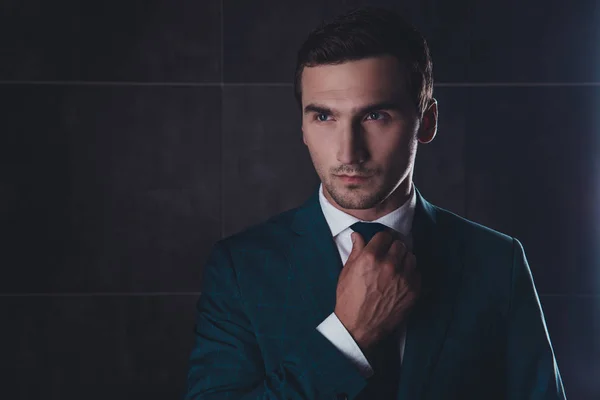 Portrait of stylish man in black suit correcting tie — Stock Photo, Image