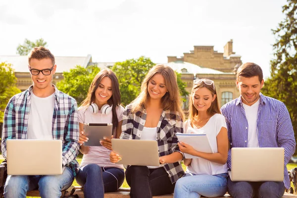 П'ять щасливих усміхнених різноманітних студентів сидять на лавці і навчаються — стокове фото