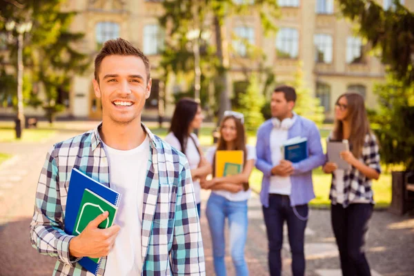 Feliz joven descanso y sosteniendo libros mientras está de pie en backgro — Foto de Stock