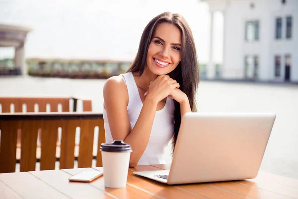 Молодая улыбающаяся женщина в кафе на открытом воздухе пьет кофе и работает — стоковое фото
