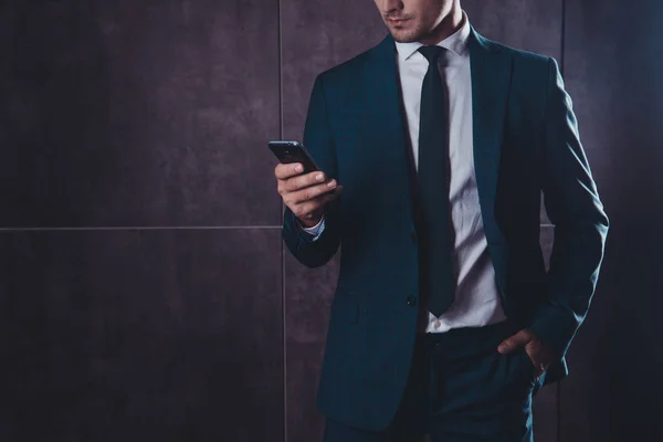Close up of businessman in black suit using smartphone on gray b — Stock Photo, Image