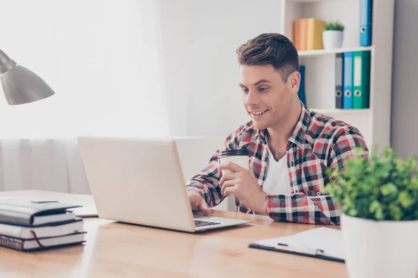 Jonge gelukkige kerel met kop koffie met behulp van laptop — Stockfoto
