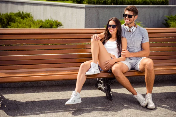 Mladý pohledný muž sedící na lavičce a huging jeho přítelkyně — Stock fotografie