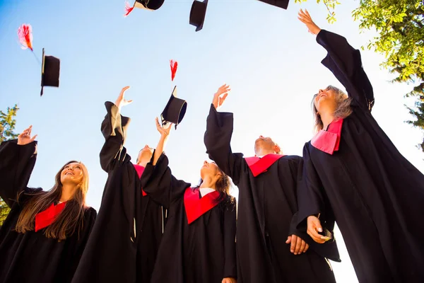Heureux groupe de jeunes diplômés jetant des chapeaux dans les airs — Photo