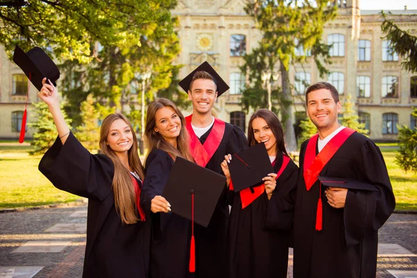 Успішні щасливі п'ять випускників в одязі та капелюхах з талісманом — стокове фото