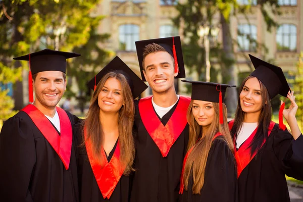 Успішні радісні п'ять випускників в одязі та капелюхах з талісманом — стокове фото