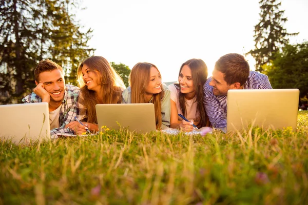 Cinque allegri migliori amici sdraiati sull'erba con i computer portatili — Foto Stock