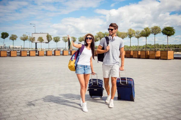 Dos jóvenes amantes sonrientes con valise caminando desde el aeropuerto hasta — Foto de Stock
