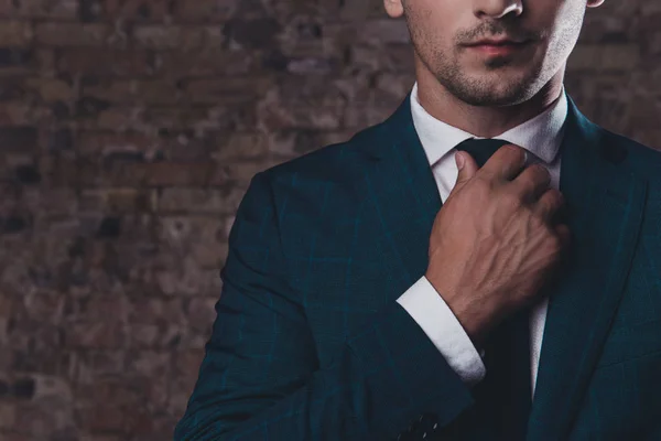 Close up of stylish man in black suit correcting tie — Stock Photo, Image
