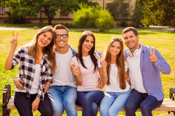 Het is vakantie! vijf vrolijke studenten zitten op bankje in groene pa — Stockfoto