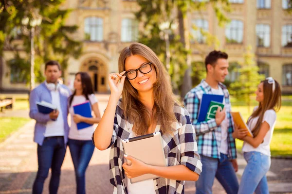Розумна щаслива дівчина стоїть поруч з університетом та її друзями та рекламою — стокове фото