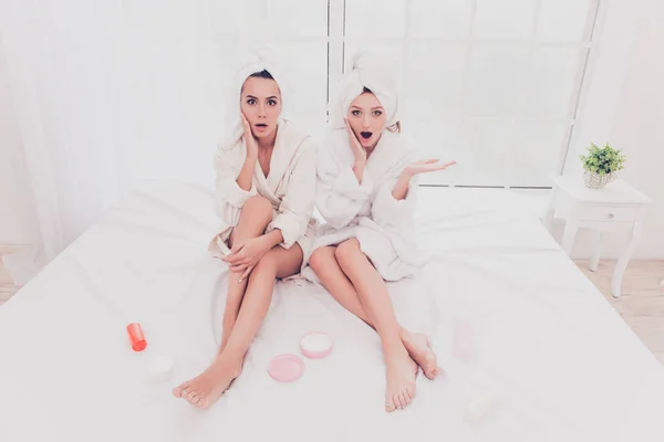 Tak bisa dipercaya! Shocked young women in bathrobes siting on bed — Stok Foto