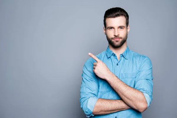 Guapo hombre barbudo sonriente apuntando hacia el fondo gris — Foto de Stock