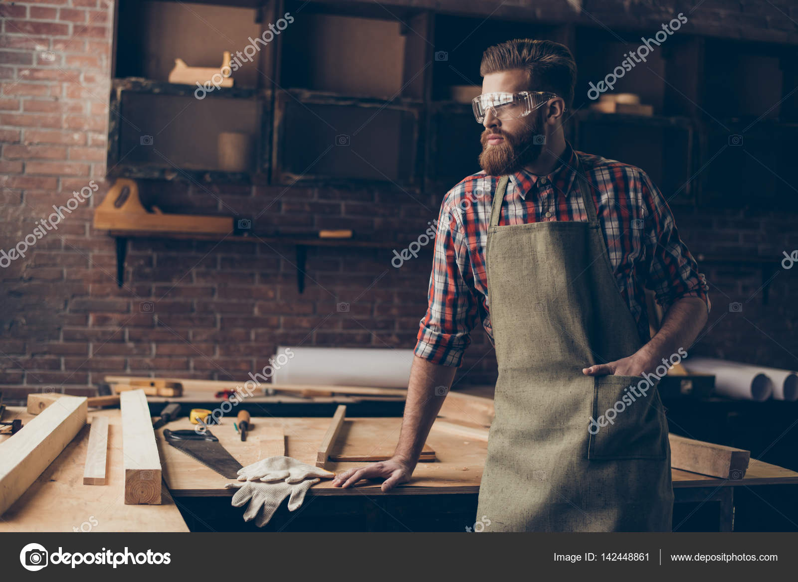 Bearded handsome joiner think and look to the side near tableto Stock