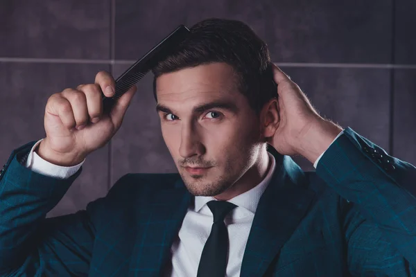 Portrait of handsome young man in black suit combing hair — Stock Photo, Image