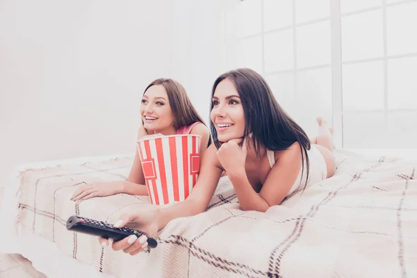 Mooie vriendinnen liggend op bed met popcorn en resta kijken — Stockfoto