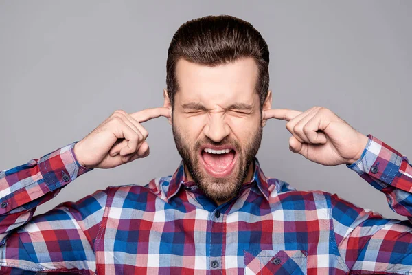 Un ritratto di un giovane uomo irritato con le dita nelle orecchie urla — Foto Stock