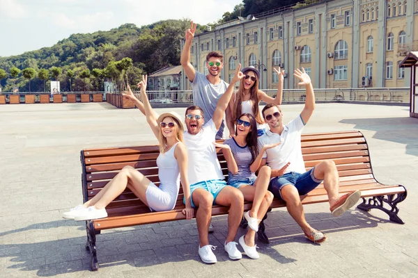 Gruppe lächelnder Freunde auf Bank sitzend und Hände winkend — Stockfoto