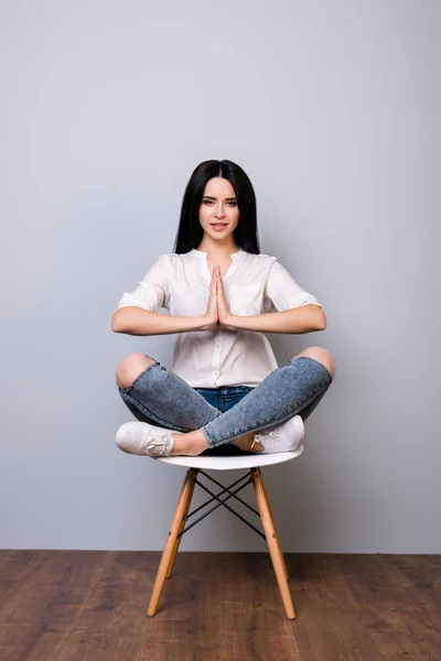 Beautiful young woman sitting on chair in lotus pose against gra — Stock Photo, Image