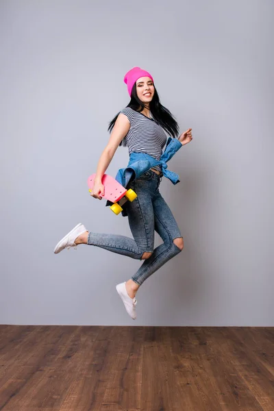 Jovem mulher na moda em jeans e chapéu rosa segurando skate e — Fotografia de Stock