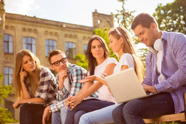 Groupe de cinq étudiants heureux assis sur le banc et parlant — Photo