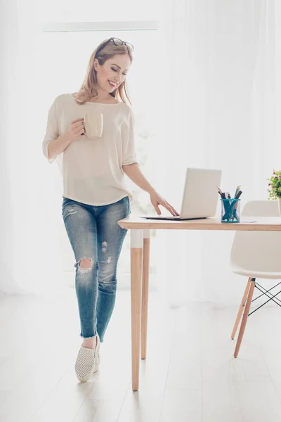 Mujer bonita joven que trabaja con el ordenador portátil de pie cerca de la mesa —  Fotos de Stock