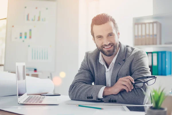 Confiado arquitecto sonriente en el desgaste formal sostiene gafas y si —  Fotos de Stock