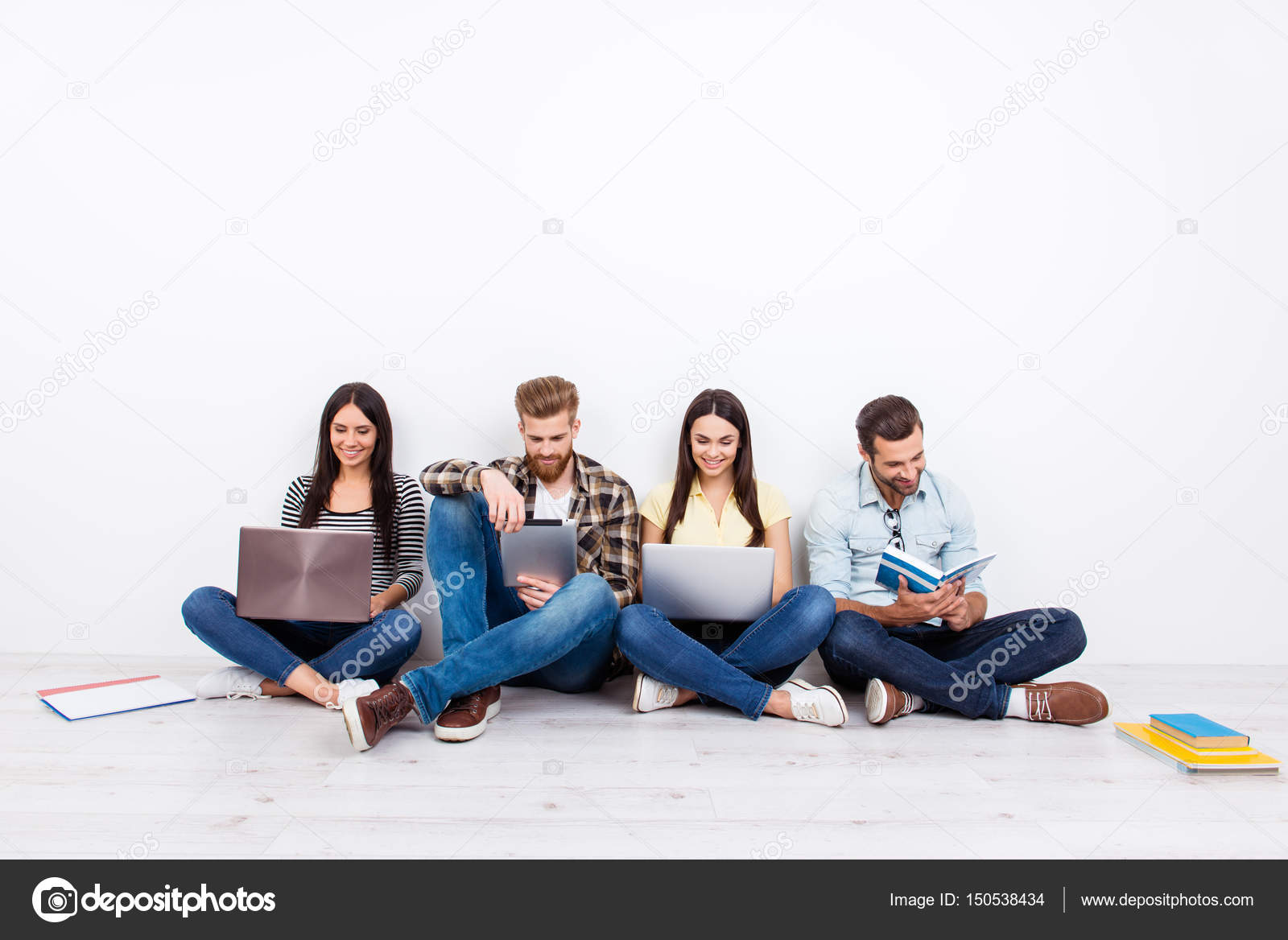 Group Of Friendly Smiling Students Sitting On The Floor And Usin