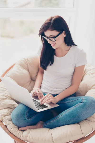 Joven bastante freelancer está sentado en un sillón acogedor y escribiendo un — Foto de Stock