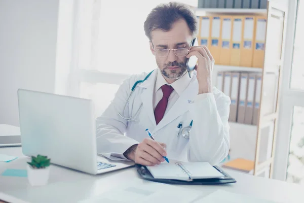 Ernstige arts raadpleegt patiënt door de telefoon en schrijven doen — Stockfoto