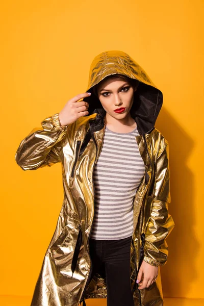 Fashionable girl wearing shining gold coat with hood on the yell — Stock Photo, Image