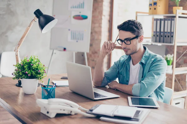 Joven chico inteligente en jeans camisa y gafas sosteniendo un lápiz i — Foto de Stock