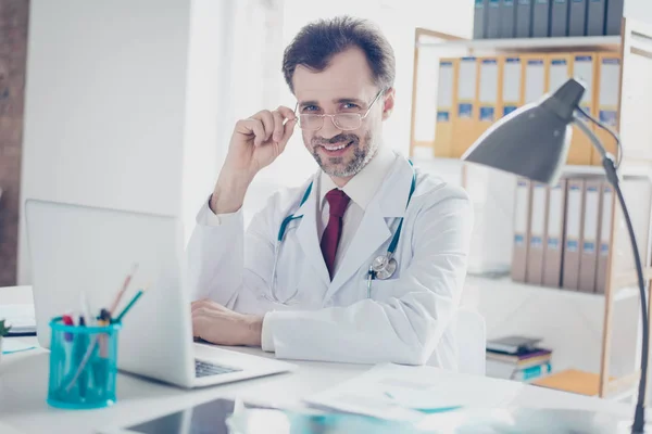 Glimlachen van de succesvolle arts zijn bril, zittend op de des vaststelling — Stockfoto