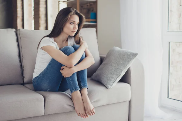 Молода досить самотня сумна дівчина сидить на дивані і обіймає коліна — стокове фото