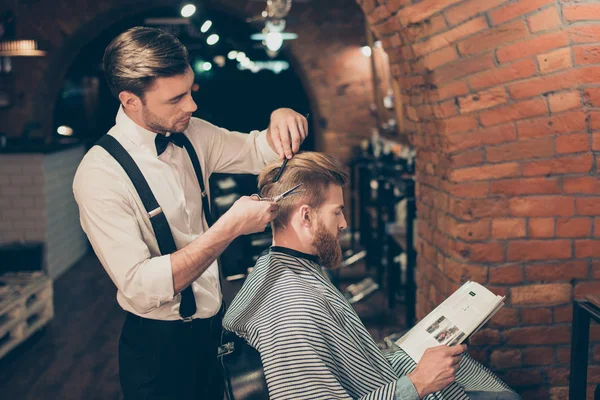 Red bearded guy is reading a magazine in a barber shop while get — Stock Photo, Image