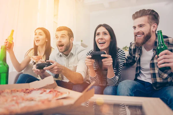 Amigos emocionados están jugando videojuegos en casa sentados en el sofá — Foto de Stock