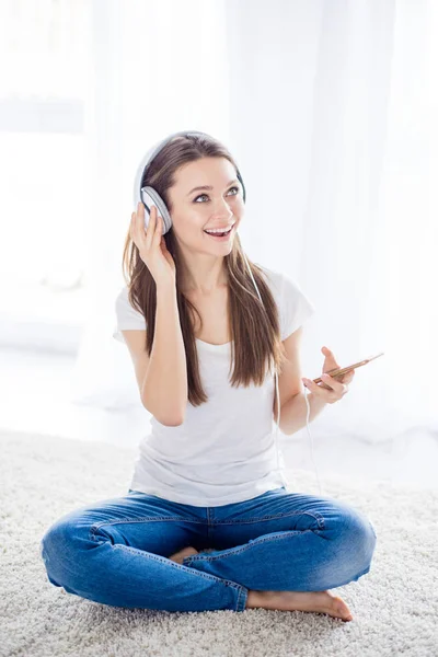 Energetic young girl listening to music in headphones sitting on Stock Image