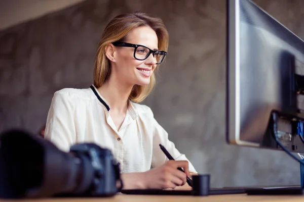 Smiling happy woman in glasses sitting at the table in front of — Stock Photo, Image