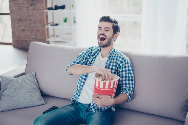 Feliz hombre riendo con camisa a cuadros comiendo palomitas de maíz mientras mira — Foto de Stock