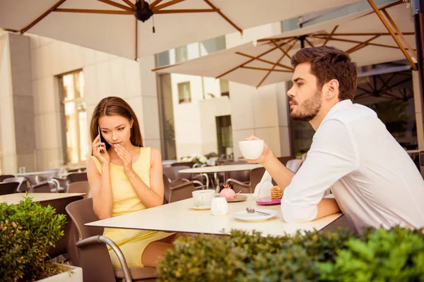 Relationship problems. Lady is talking very quiet on her smart phone, covering her mouth with the palm of hand, whille sitting on a date with guy — Stock Photo, Image