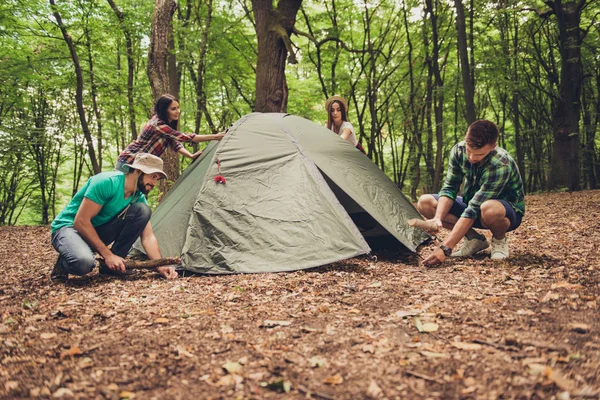 Quatro jovens amigos alegres estão montando uma tenda na floresta — Fotografia de Stock